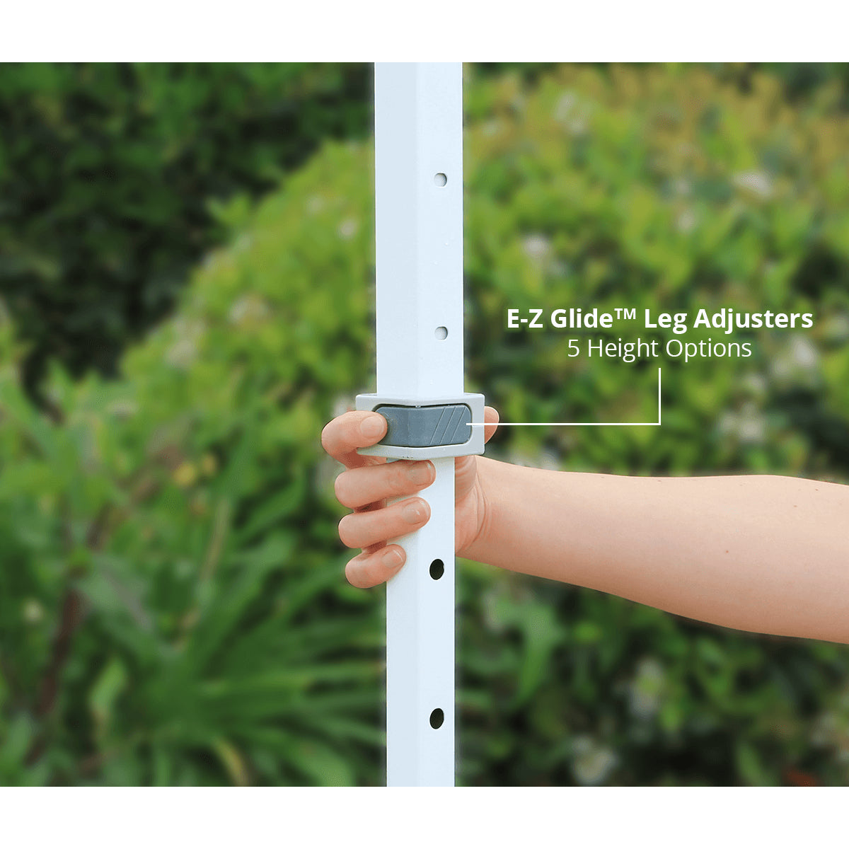 Hand using E-Z Glide leg adjuster on a white pole with green foliage in the background